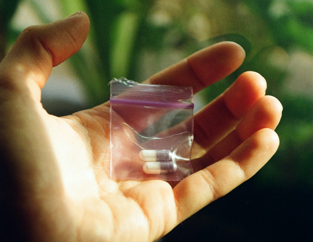 A hand holds a small clear plastic baggy containing two pills