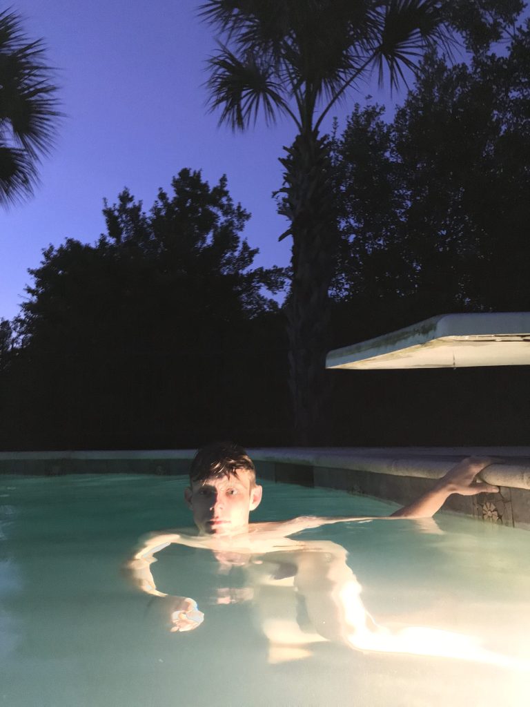 A naked white man in a swimming pool at night