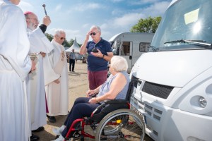 Catholic priests in the village of Malestroit, Brittany, France bless an elderly couple with gray hair and their white camper van